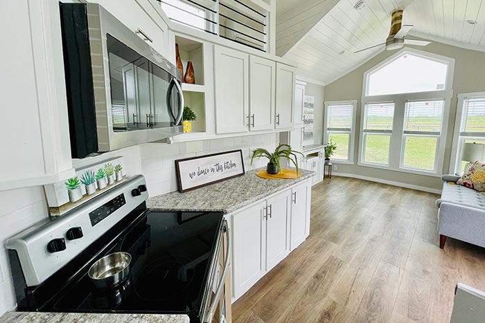 Summit tiny home modern open-plan kitchen and living room with white cabinets, large windows and wooden flooring.