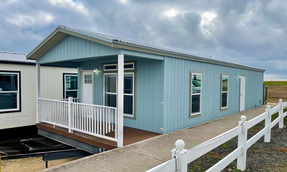 Exterior of Landmark RV Park Model home, Light blue house with a porch and white railing, under a cloudy sky.