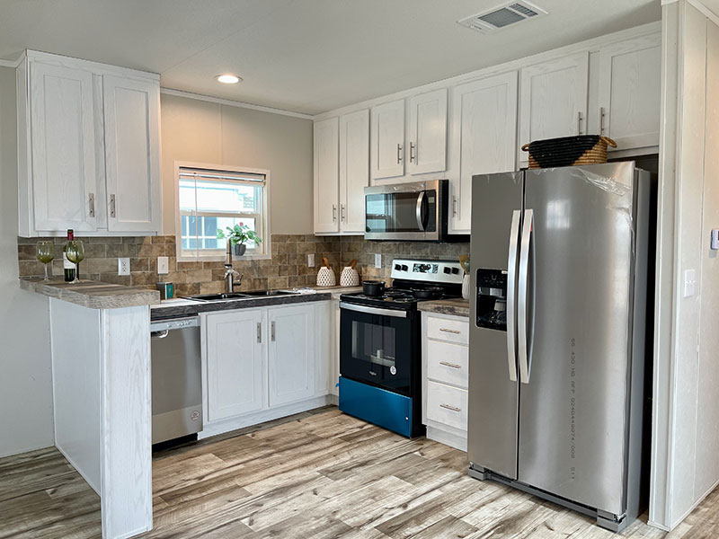 Landmark RV Park Model home, Modern kitchen with white cabinets, stainless steel appliances and a light wood floor.