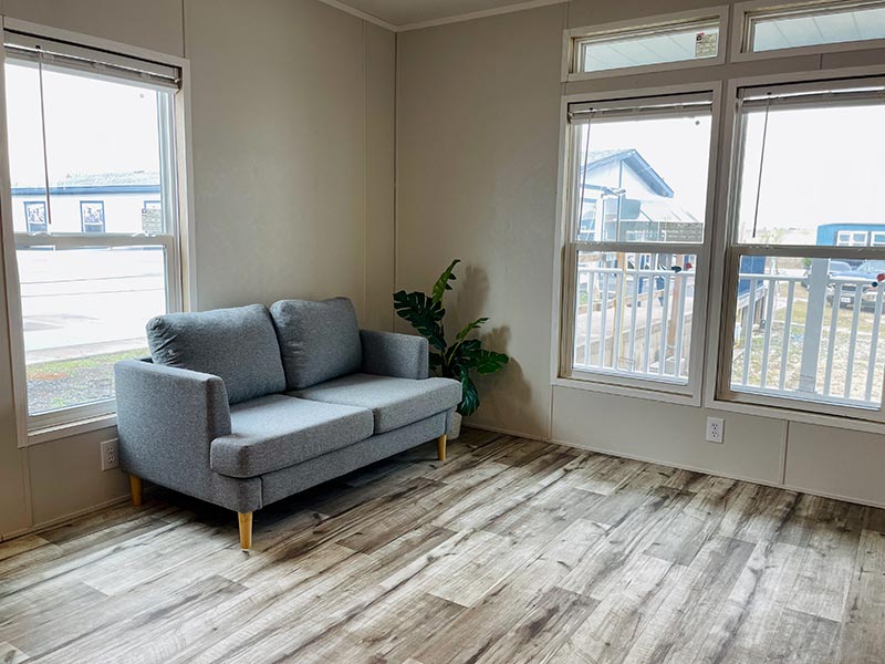 Landmark RV Park Model home, Modern living room with a gray sofa, wooden floor, large windows and a potted plant.