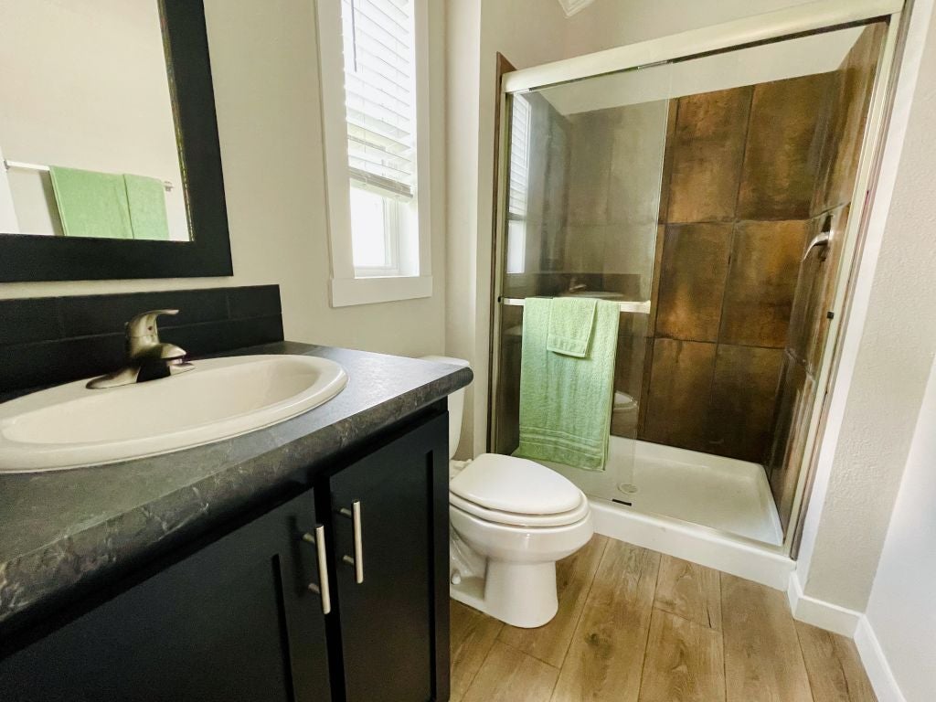 Hill Country RV Park Model tiny home modern bathroom featuring a dark wood vanity with a black countertop, a circular sink, a mirror, and a glass-enclosed shower with brown tile.