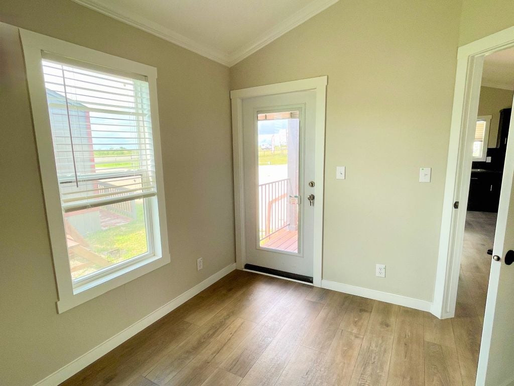 Hill Country RV Park Model tiny home Bedroom with a large window and a glass door leading outside, featuring light wooden flooring and neutral-colored walls.