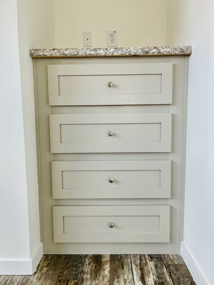 Crane RV Park Model tiny home Light gray corner cabinet with four drawers and a speckled granite countertop, set against a white wall and wooden flooring.