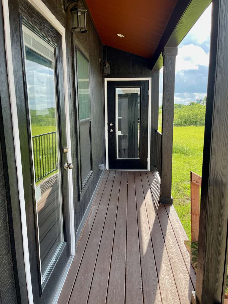 Hill Country RV Park Model tiny home narrow, dark wooden porch with a black door and two large glass-panel doors on the left side, under a sloped orange ceiling.
