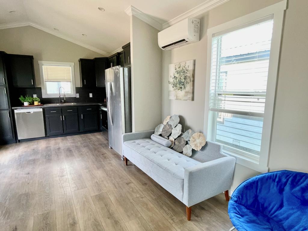 Hill Country RV Park Model tiny home modern kitchen and Living Room featuring dark cabinetry, stainless steel appliances, a light gray tufted sofa, and decorative coral-like accents.
