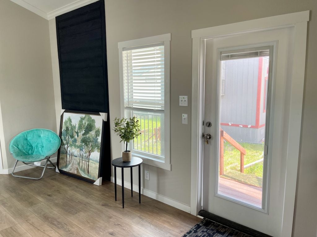 Hill Country RV Park Model tiny home Interior view of a Living room with a teal chair, a landscape painting, a potted plant on a black table, and a glass door leading to a deck.
